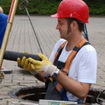 Mann mit rotem Helm und Arbeitskleidung steht in Abwasserschacht
